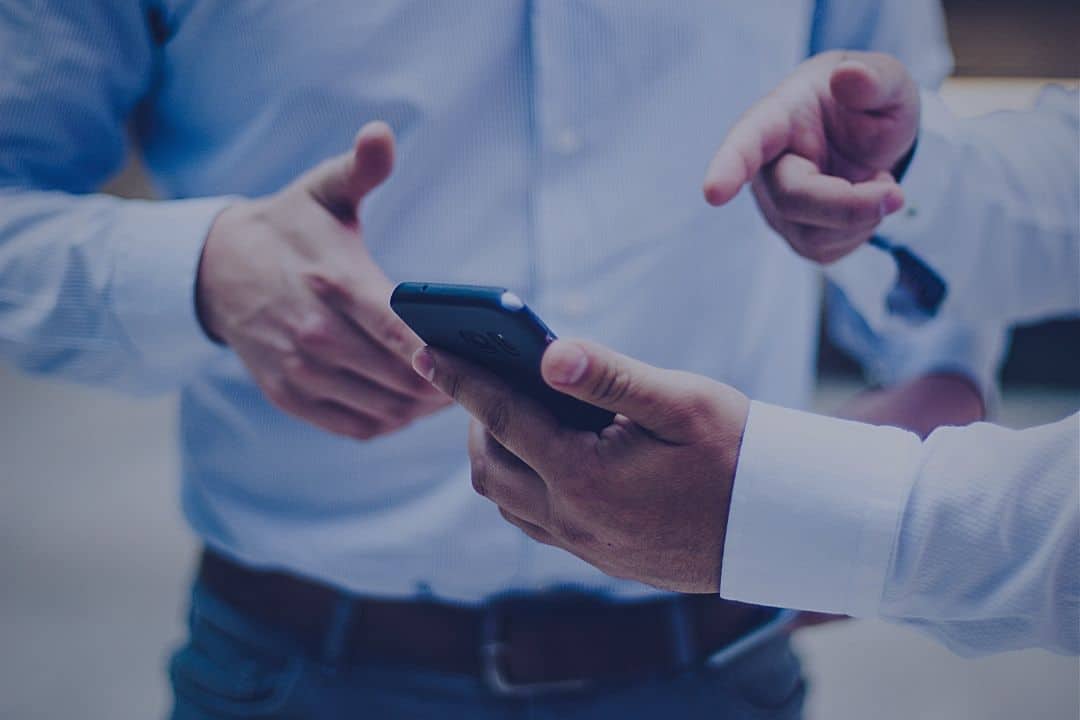 man pointing to smartphone screenwhile talking to another man