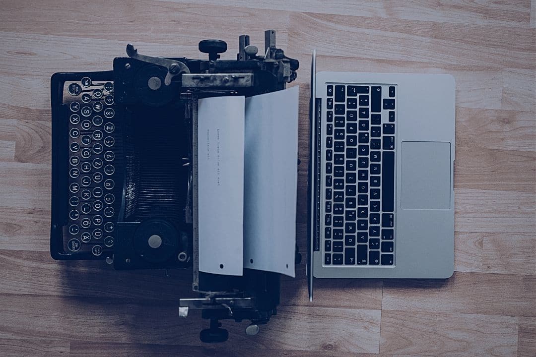 laptop and typewriter sitting back to back on table