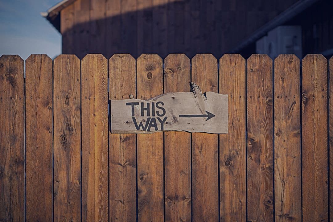 sign reading "this way" with right pointing arrow hanging on wooden fence