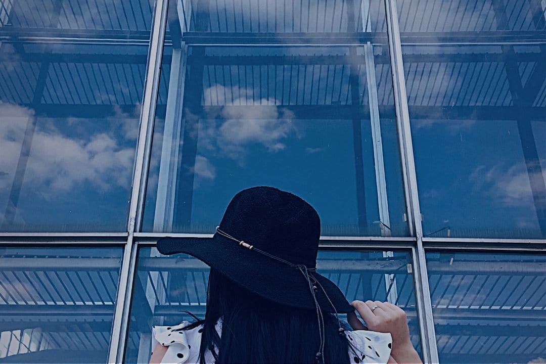 woman staring up at clouds reflected in office window