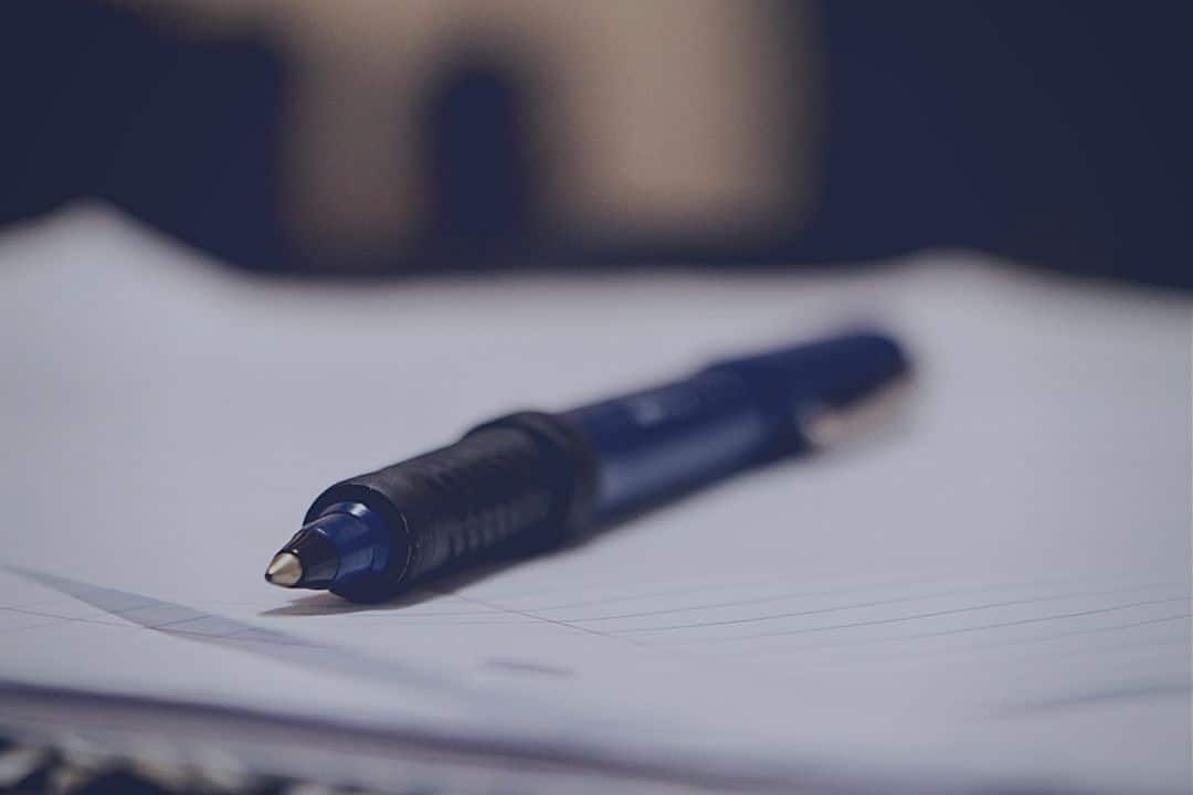 closeup of blue pen sitting on white notebook