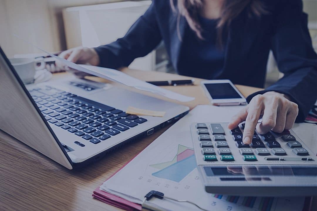 Woman working on calculator and computer at the same time.