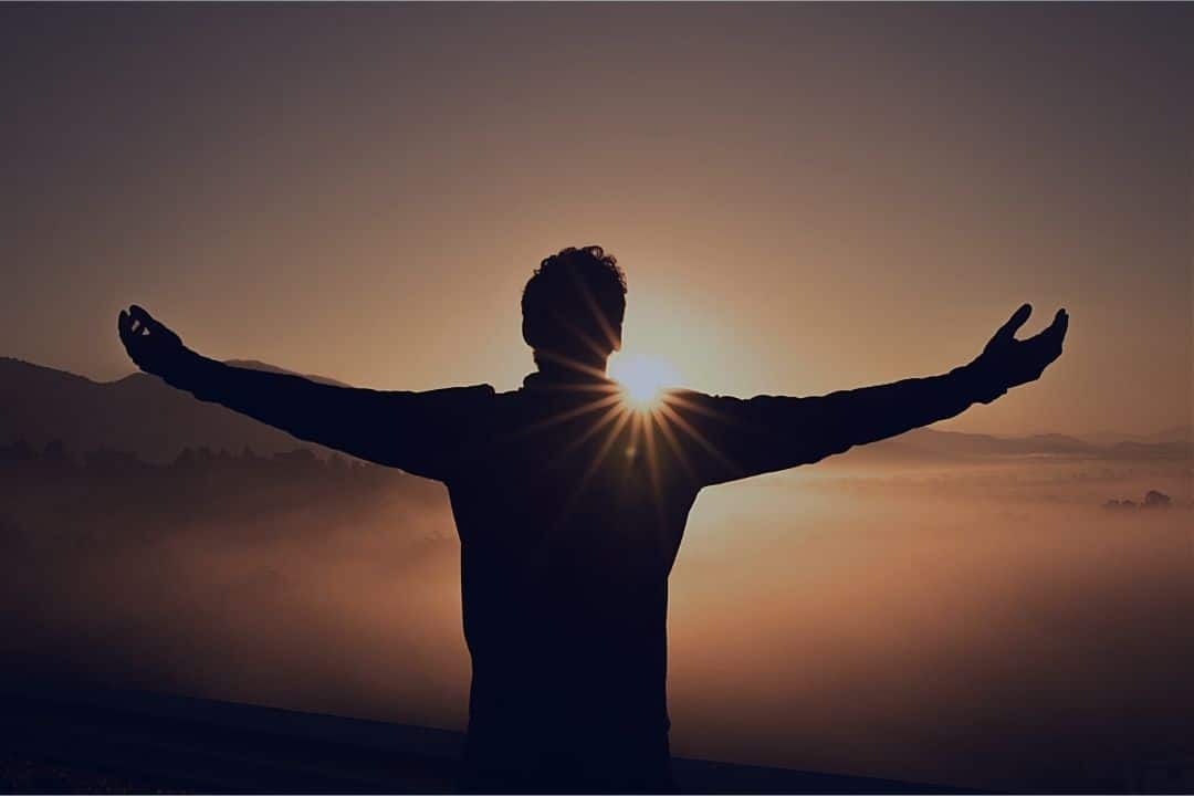 Man reaching out in front of the sunrise