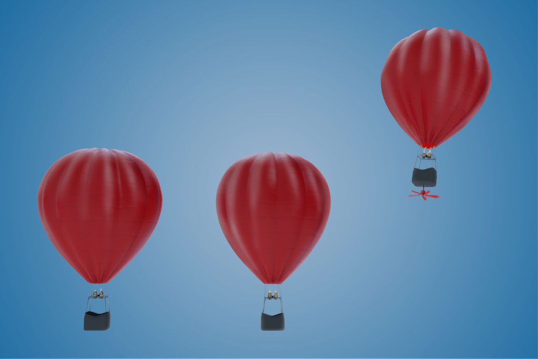 3 hot air balloons in the sky. One, with a fan underneath is flying higher than the others.