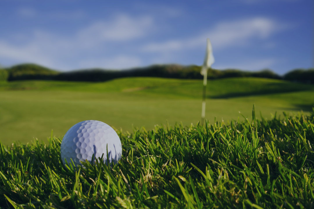 Golf ball stuck in rough grass with hole in the distance.